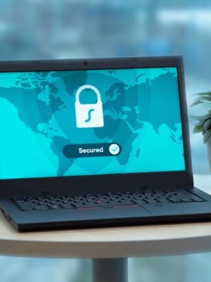 Laptop z ikoną kłódki na ekranie stoi na stole obok rośliny.