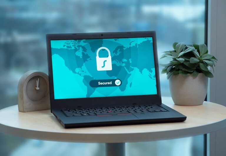 Laptop z ikoną kłódki na ekranie stoi na stole obok rośliny.