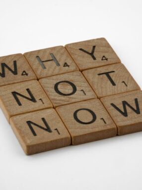Drewniane płytki z literami ułożone w słowa "WHY", "NOT", "NOW".