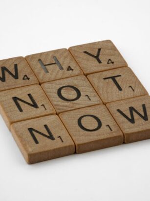 Drewniane płytki z literami ułożone w słowa "WHY", "NOT", "NOW".
