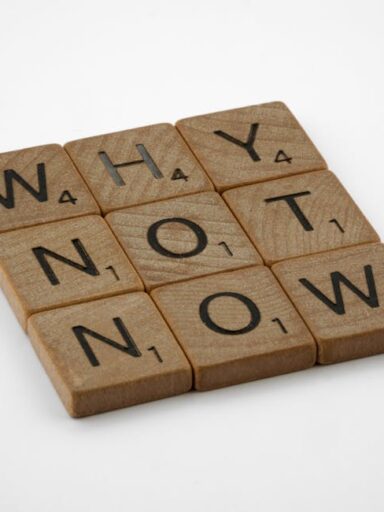 Drewniane płytki z literami ułożone w słowa "WHY", "NOT", "NOW".