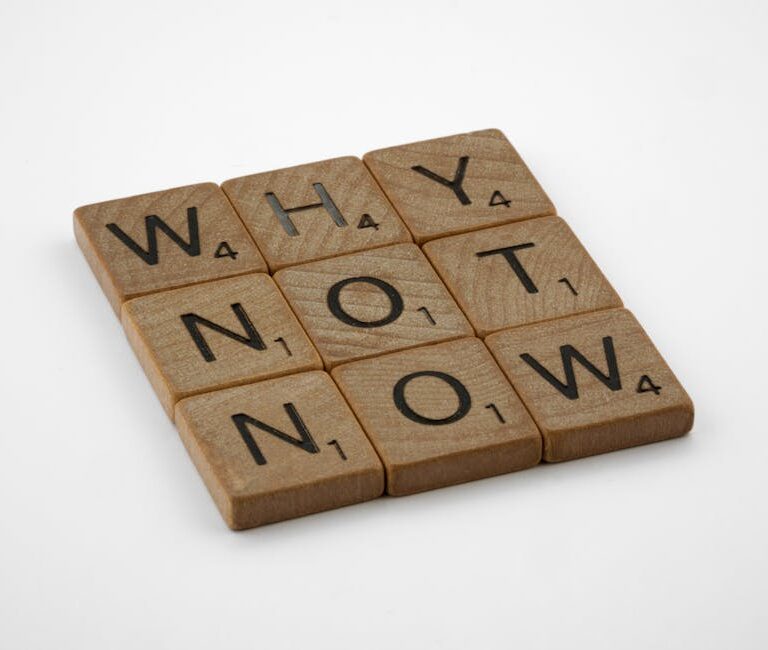 Drewniane płytki z literami ułożone w słowa "WHY", "NOT", "NOW".