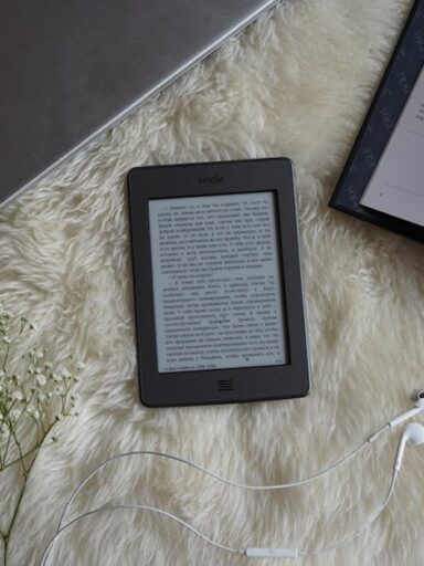 Czytnik e-booków, laptop, otwarta książka i kwiaty na futrzanym kocu.