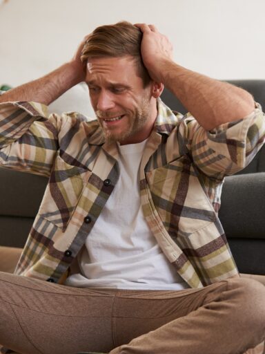 mężczyzna siedzący na podłodze i zasłaniający uszy