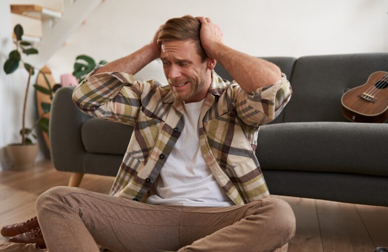 mężczyzna siedzący na podłodze i zasłaniający uszy