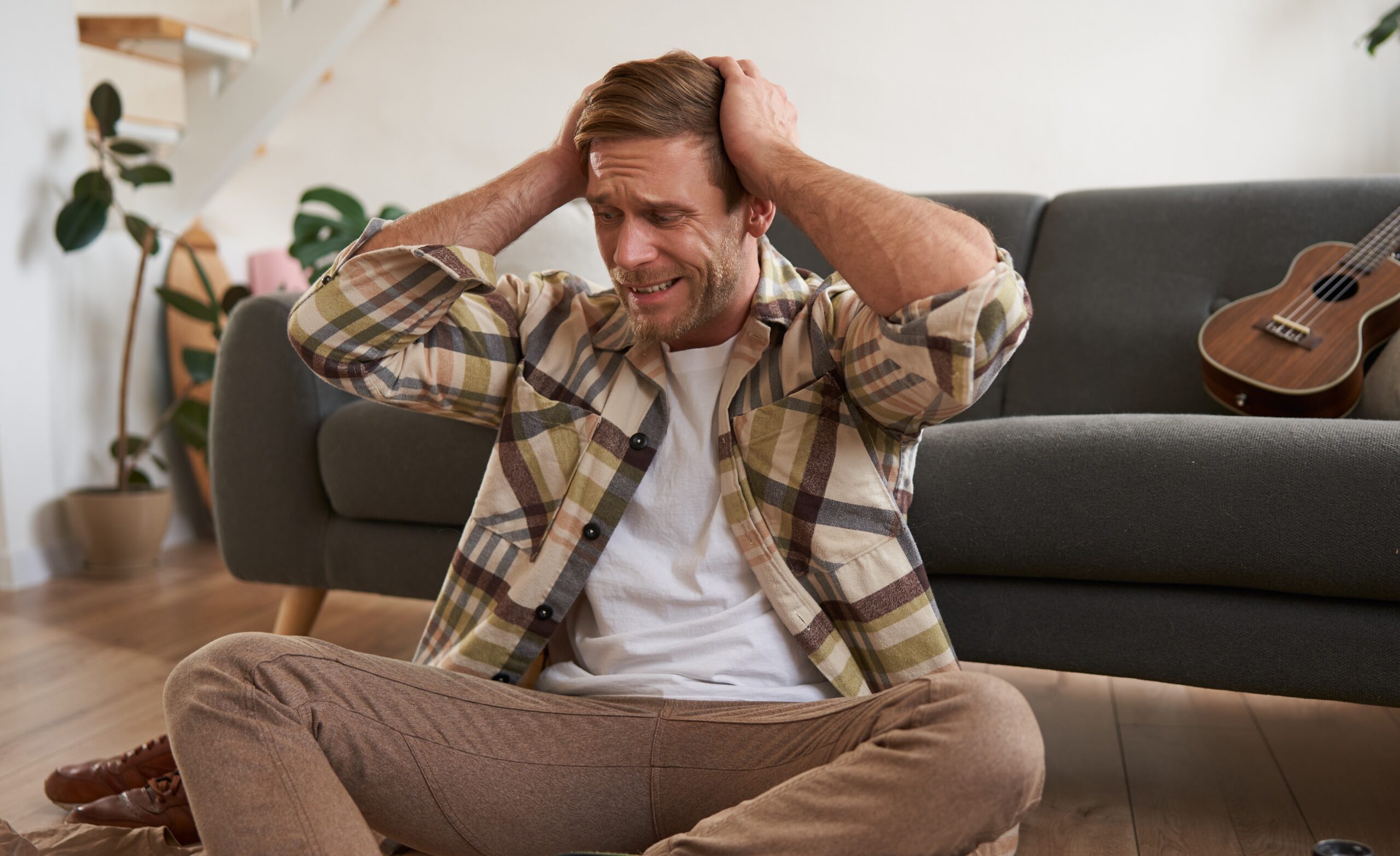 mężczyzna siedzący na podłodze i zasłaniający uszy