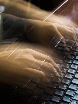 Rozmyte dłonie osoby piszącej na klawiaturze starego laptopa.