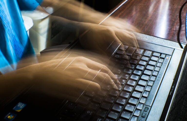 Rozmyte dłonie osoby piszącej na klawiaturze starego laptopa.