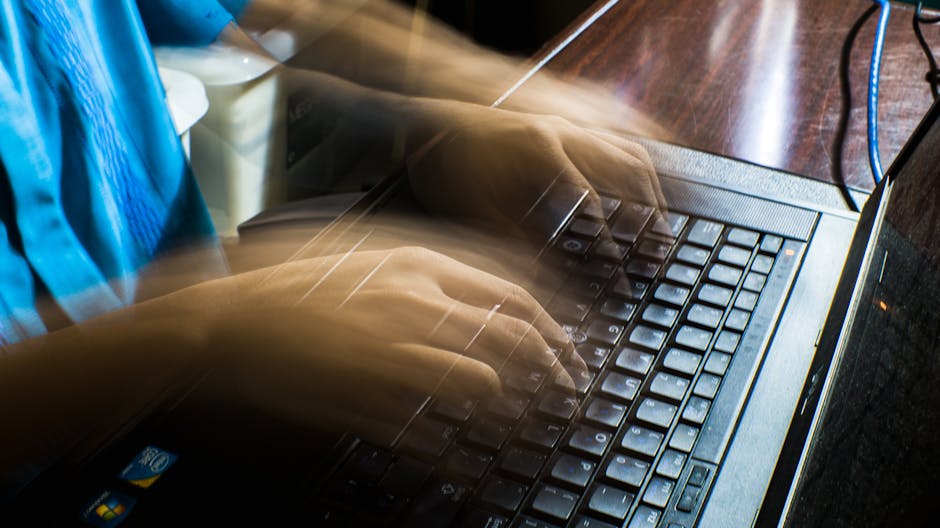 Rozmyte dłonie osoby piszącej na klawiaturze starego laptopa.