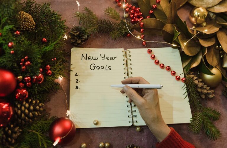Ręka z długopisem nad otwartym notatnikiem z napisem New Year Goals.
