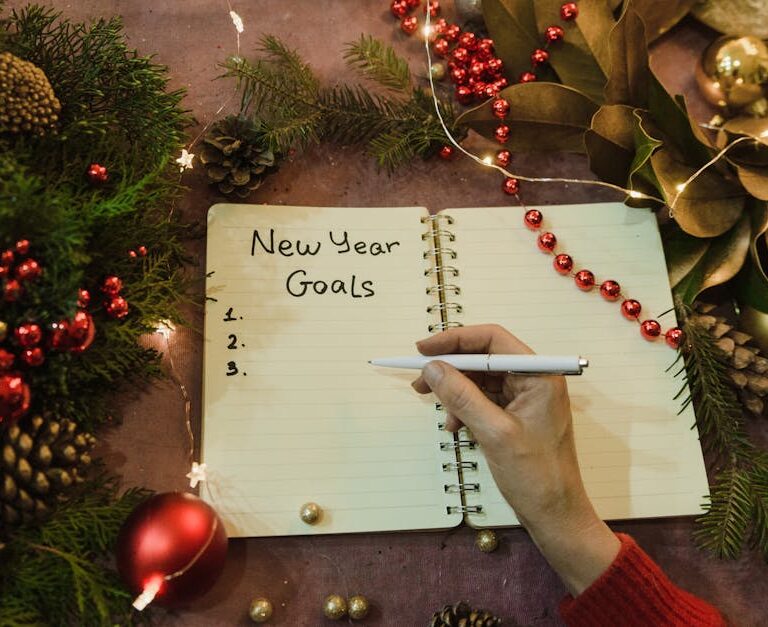 Ręka z długopisem nad otwartym notatnikiem z napisem New Year Goals.