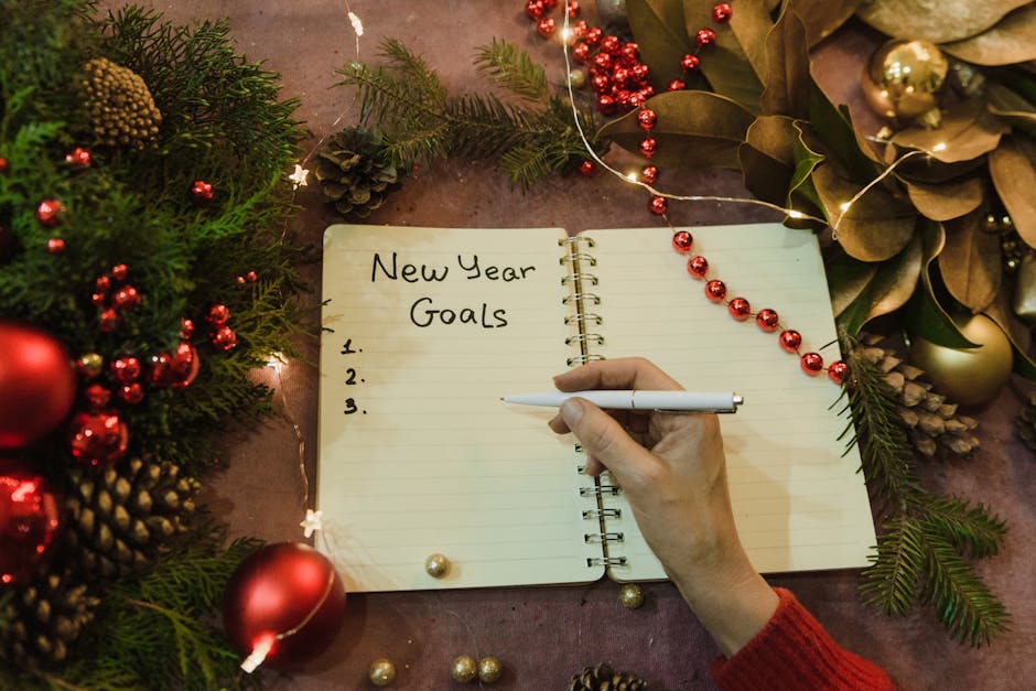 Ręka z długopisem nad otwartym notatnikiem z napisem New Year Goals.