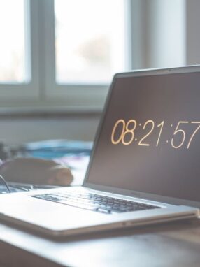 Laptop z wyświetlonym czasem 08:21:57 na biurku przy oknie.