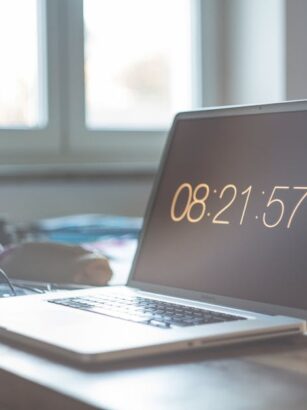 Laptop z wyświetlonym czasem 08:21:57 na biurku przy oknie.