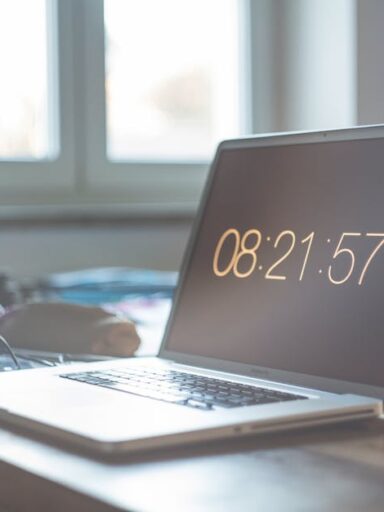 Laptop z wyświetlonym czasem 08:21:57 na biurku przy oknie.