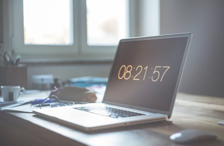 Laptop z wyświetlonym czasem 08:21:57 na biurku przy oknie.