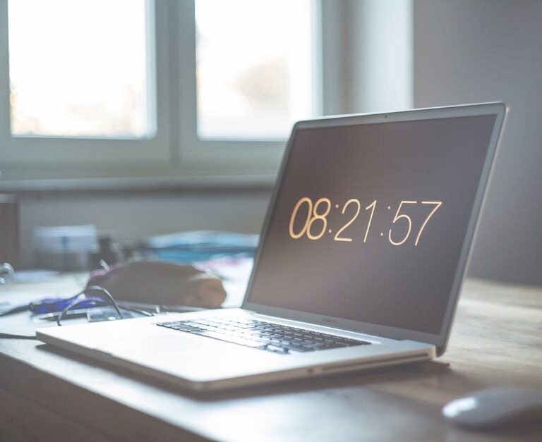 Laptop z wyświetlonym czasem 08:21:57 na biurku przy oknie.