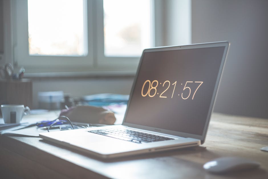 Laptop z wyświetlonym czasem 08:21:57 na biurku przy oknie.