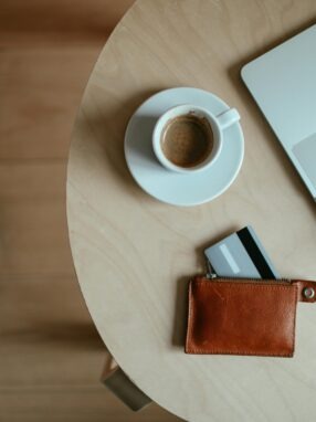 laptop, kawa i portfel z wysuniętą kartą na stoliku