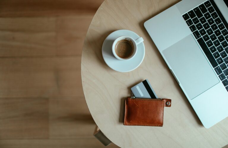 laptop, kawa i portfel z wysuniętą kartą na stoliku