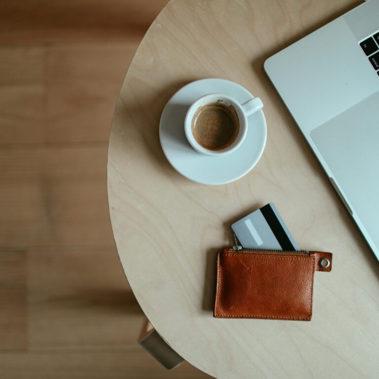 laptop, kawa i portfel z wysuniętą kartą na stoliku