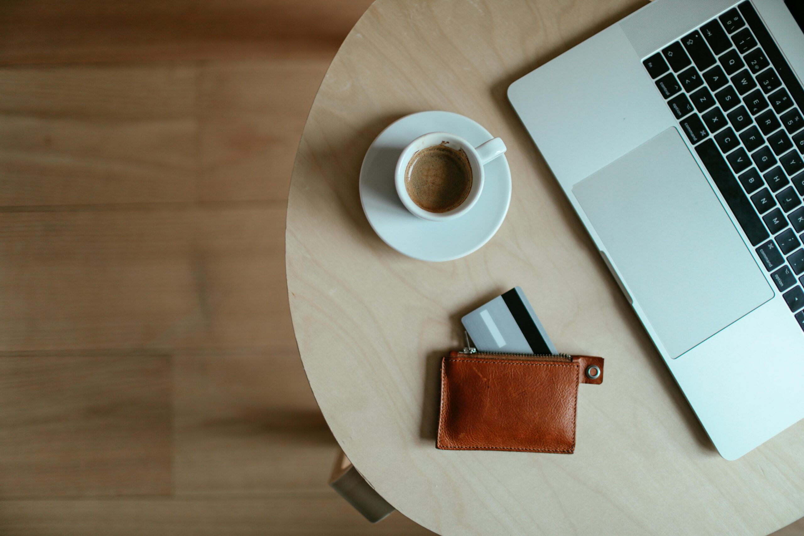 laptop, kawa i portfel z wysuniętą kartą na stoliku