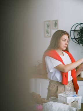 Kobieta wkłada szklaną butelkę do pojemnika z napisem GLASS w kuchni.