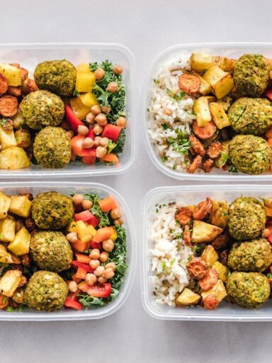 Cztery plastikowe pojemniki wypełnione daniem z falafelami, ryżem i pieczonymi warzywami.